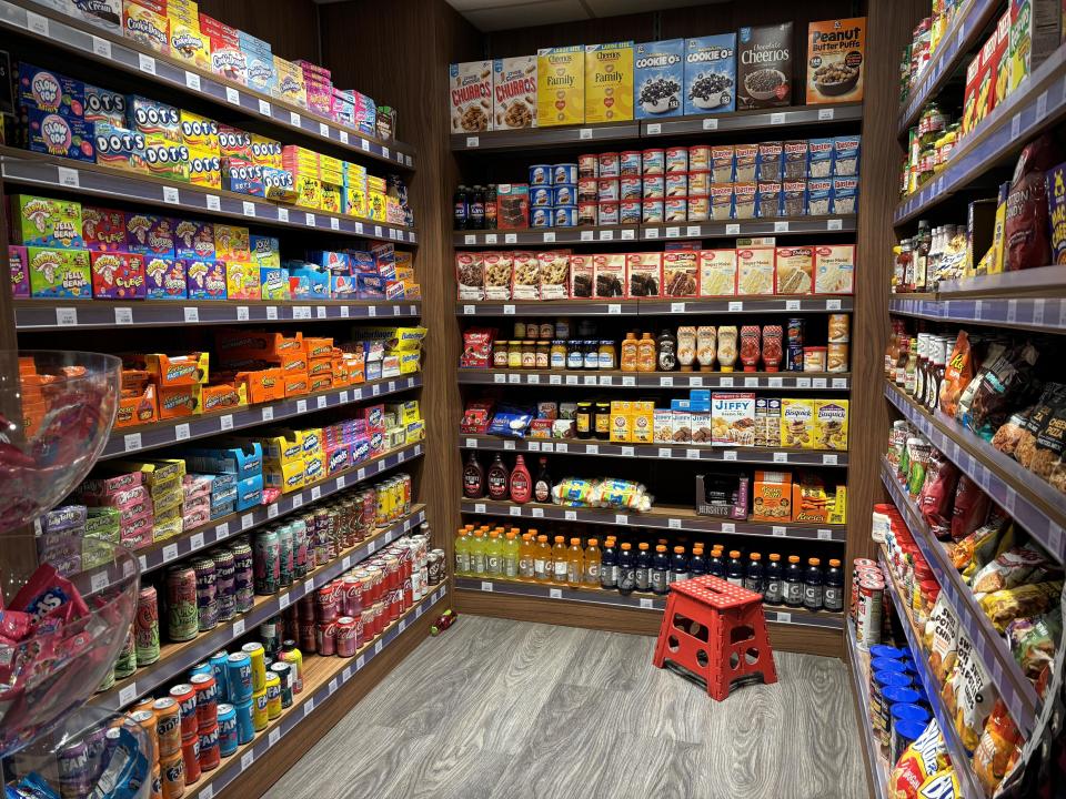 A fully stocked grocery store aisle with various snacks, cereals, and beverages. A red step stool is on the floor. No people are present