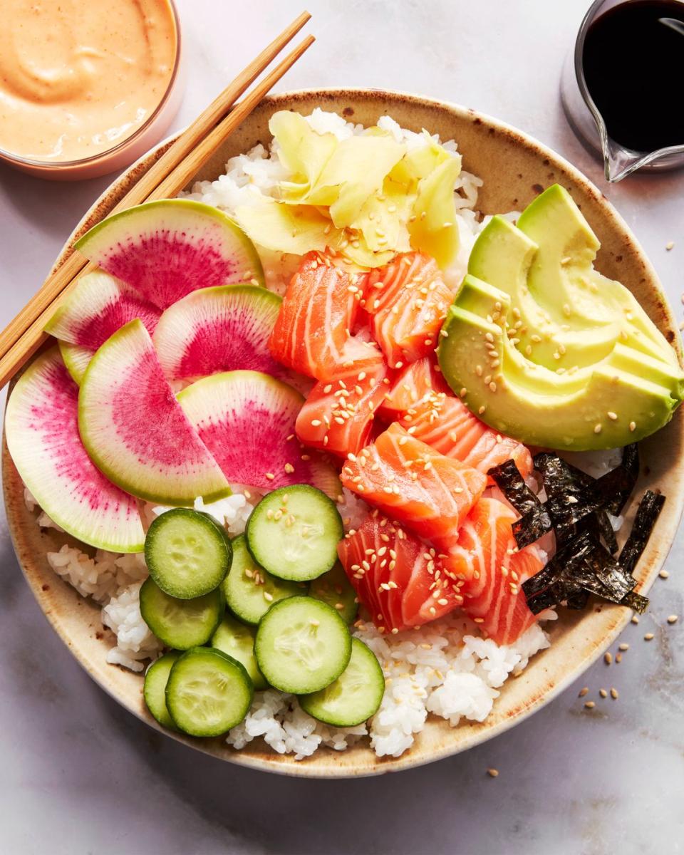 sushi rice in a bowl topped with salmon, cucumber, watermelon radish, sliced avocado, and spicy mayo