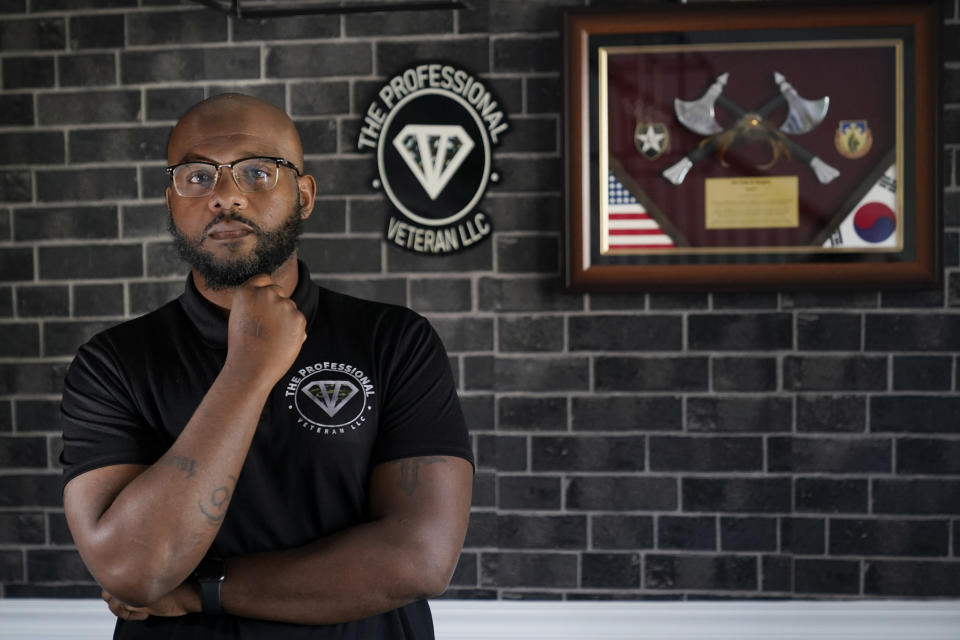 Phillip Slaughter, who served in the U.S. Army for 18 years, poses in his home Nov. 10, 2022, in Clarksville, Tenn. Framed on his wall on the right are memorabilia from a military assignment in South Korea where he worked as a logistics trainer. On the left is the logo for his company in which he helps service members transition into the civilian workforce. (AP Photo/Mark Humphrey)