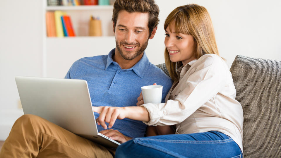 couple sitting on couch and happily looking at laptop