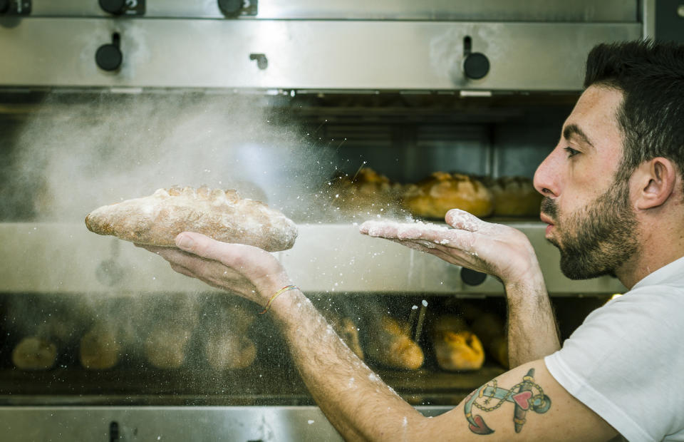 A chef is blowing the flour from baked bread