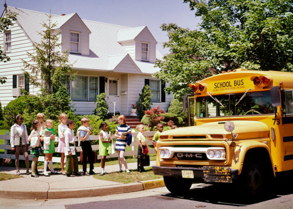 Children lining up to board a yellow school bus on a suburban street