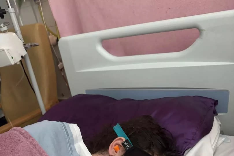 Millie in hospital lying down with an eye mask on and her teddy