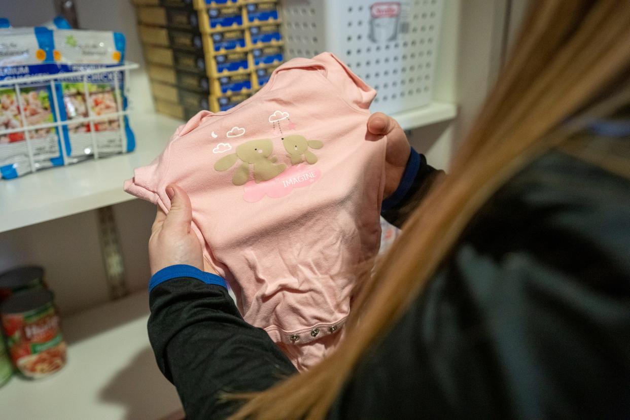 Community Health Worker Mariah Sharpe holds a onesie that is part of the offerings given to new mothers as part of their donation program at the OhioHealth Castrop Health Center in Athens, Ohio.