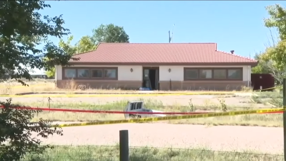 A one-story building with boarded-up windows, surrounded by police tape