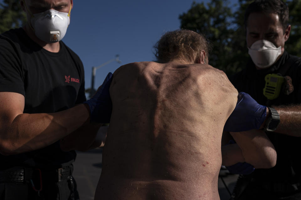 Cody Miller, right, with the Salem Fire Department, along with Falck Northwest ambulance personnel, treats a man experiencing heat exposure at a cooling center during a heat wave, Saturday, June 26, 2021, in Salem, Ore. (AP Photo/Nathan Howard)