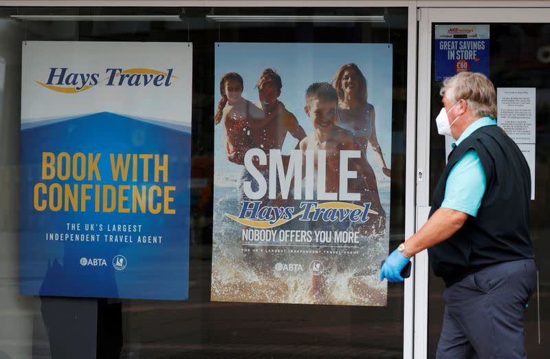 Man wearing a protective face mask walks past a travel agents store, in Manchester