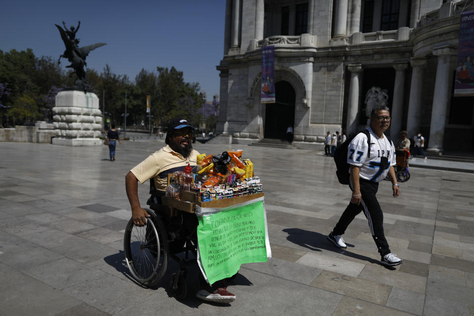 Guillermo Gonzalez Sanchez sells cigarettes and snacks from atop his wheelchair, outside the Palace of Fine Arts in downtown Mexico City, Tuesday, March 24, 2020. Gonzalez, who doesn't believe the new coronavirus is real, says the threat is just the latest tactic to suppress the Mexican people, many of whom like him live from day to day. (AP Photo/Rebecca Blackwell)