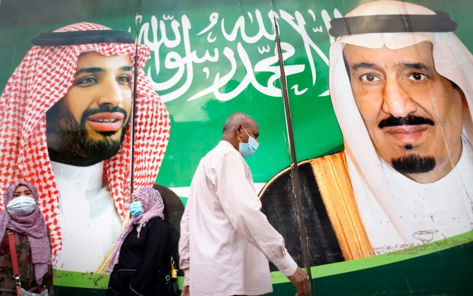 People wear masks in front of a banner showing Saudi King Salman, right, and his Crown Prince Mohammed bin Salman, outside a mall in Jiddah, Saudi Arabia - Amr Nabil/AP