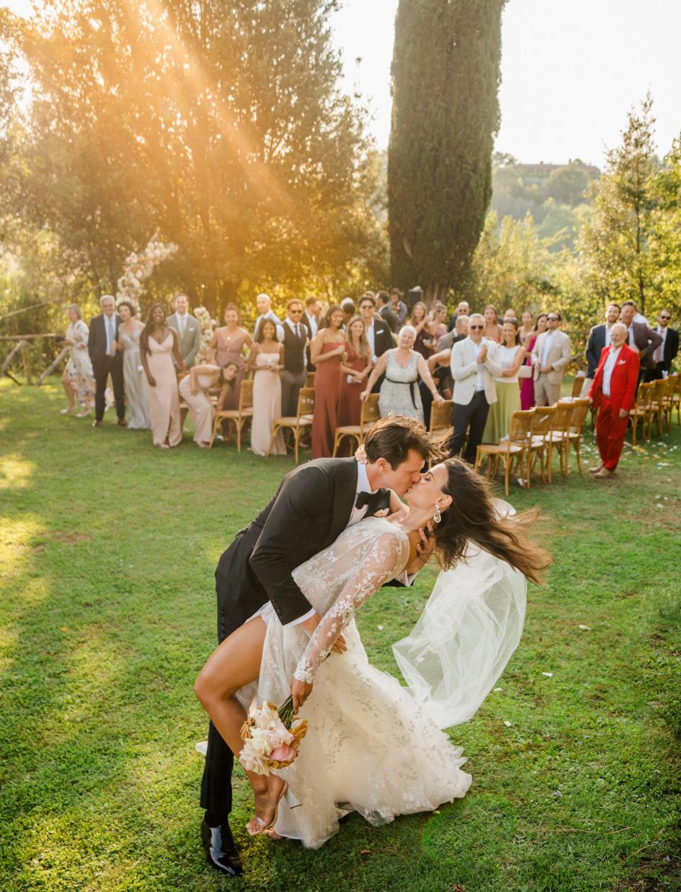 A groom dips and kisses his bride as their wedding guests celebrate them.