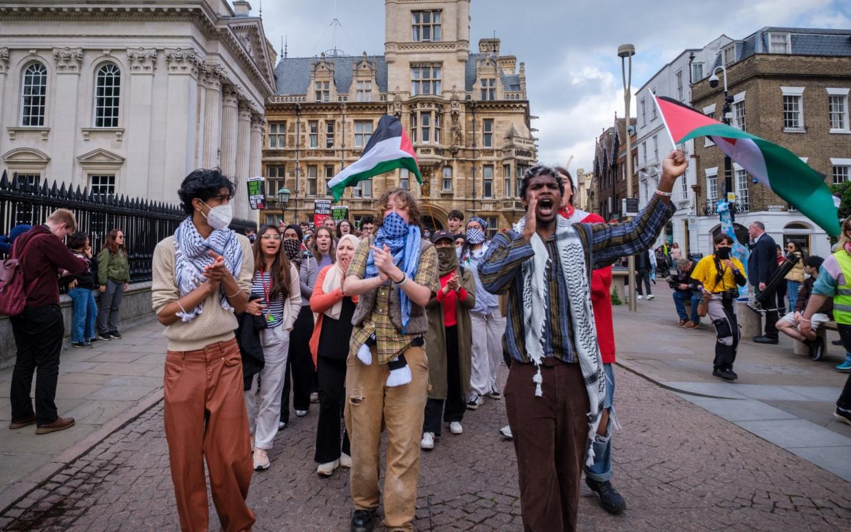 A group of young people walk towards the camera with banners and wearing Palestinian scarves