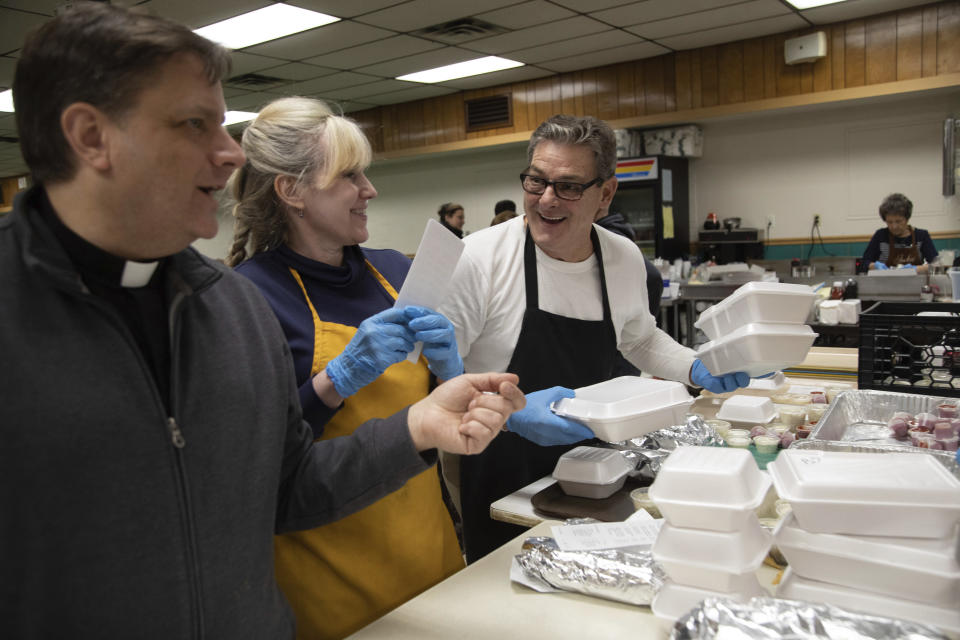In this Feb. 28, 2020 photo, from left, Father Steve Kresak, parish priest at Holy Angels, jokes with Lisa Cotter and Joe Bilock as they prepare meals during the fish fry at Holy Angels parish in Pittsburgh. The church sells 2,000 pounds of fish each Friday during Lent. On March 12, Pittsburgh Bishop David Zubik suggested that people enjoy the fish fries with a take-out order rather than dining in due to virus concerns. (AP Photo/Rebecca Droke)