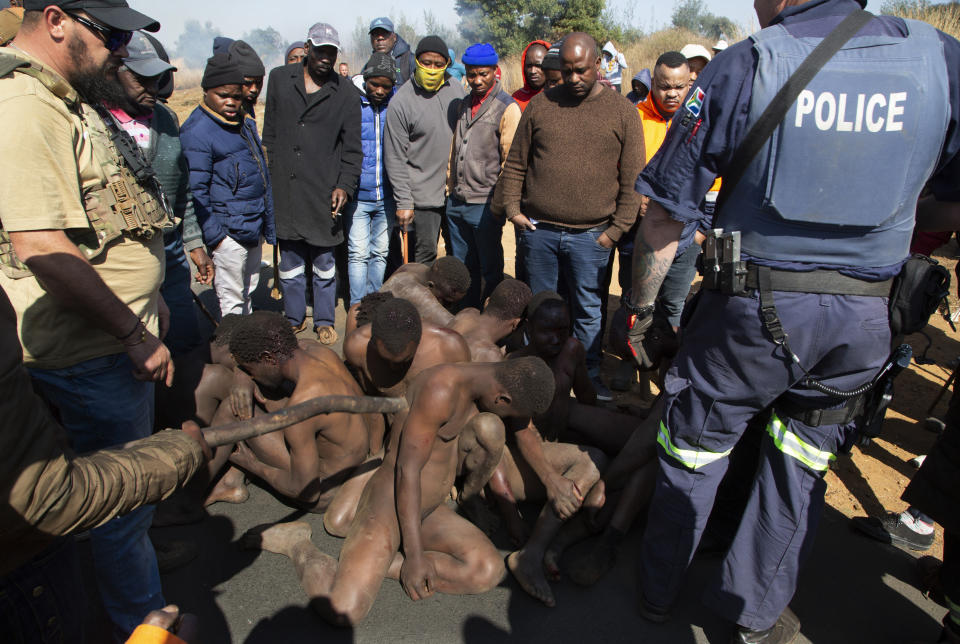 Residentes rodean a presuntos mineros ilegales de oro después de golpearlos y desnudarlos antes de que la policía los arrestara cerca de Krugersdorp, Sudáfrica, el 4 de agosto de 2022. Los hombres fueron golpeados con palos y sus campamentos incendiados luego de las presuntas violaciones grupales de ocho mujeres por parte de mineros la semana anterior. (AP Foto/Denis Farrell)