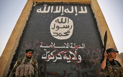 Fighters from the Hashed al-Shaabi (Popular Mobilisation units), backing the Iraqi forces, stand in front of a mural depicting the emblem of the Islamic State (Isil) group as troops advance through Hawija - Credit: AFP