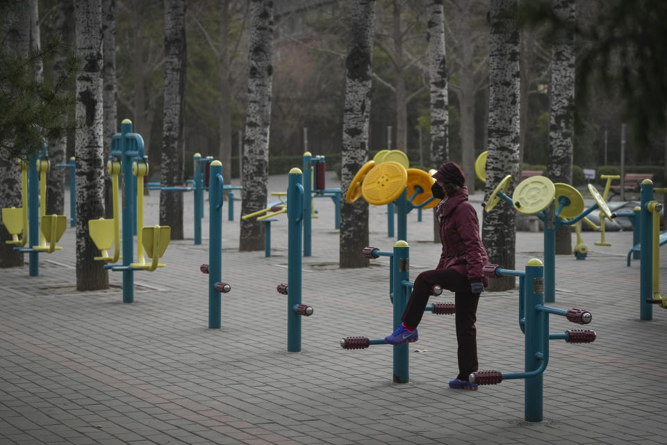 A masked resident massages her leg at a quiet gym equipments area inside a public park in Beijing, Monday, Dec. 12, 2022. China will drop a travel tracing requirement as part of an uncertain exit from its strict "zero-COVID" policies that have elicited widespread dissatisfaction. (AP Photo/Andy Wong)