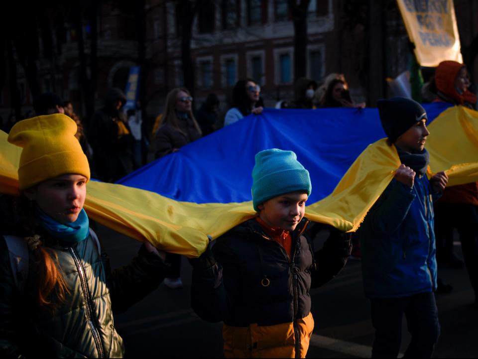Young Romanians in Bucharest hold a Ukraine flag (Andreea Alexandru/AP)