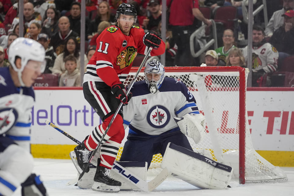 Chicago Blackhawks right wing Taylor Raddysh (11) runs into Winnipeg Jets goaltender Connor Hellebuyck, right, drawing a penalty, during the second period of an NHL hockey game Friday, Feb. 23, 2024, in Chicago. (AP Photo/Erin Hooley)