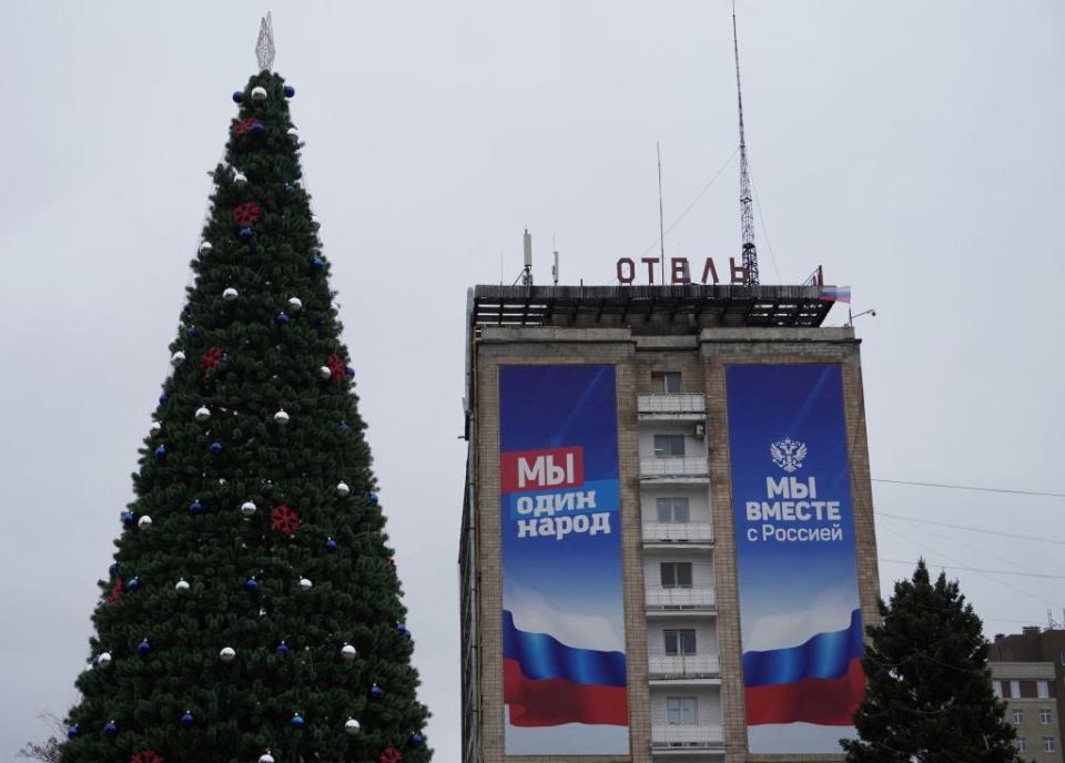 A photo taken on December 18, 2022 shows a Christmas tree in front of a building with banners reading "We are one people" and "We are together with Russia" in occupied Melitopol. (Photo by STRINGER / AFP) (Photo by STRINGER/AFP via Getty Images)