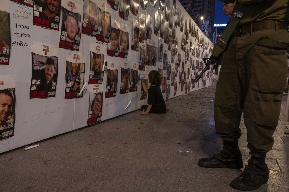 FILE - A young boy paints on a wall next to photos of Israelis missing and held captive by Hamas Militants in Tel Aviv, on Saturday Oct. 21, 2023. One of the missing, Ohad Munder-Zichri, turned 9 on Monday. But instead of celebrating at home with his family and friends, he was somewhere in Gaza, one of more than 200 Israelis held hostage by Hamas since their devastating Oct. 7 incursion. (AP Photo/Petros Giannakouris, File)