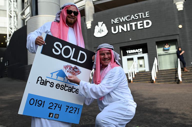 Hinchas de Newcastle vestidos con ropas árabes y un cartel de "vendido" en la puerta del club, en las afueras de St. James Park, tras el traspaso a un consorcio dominado por Arabia Saudita