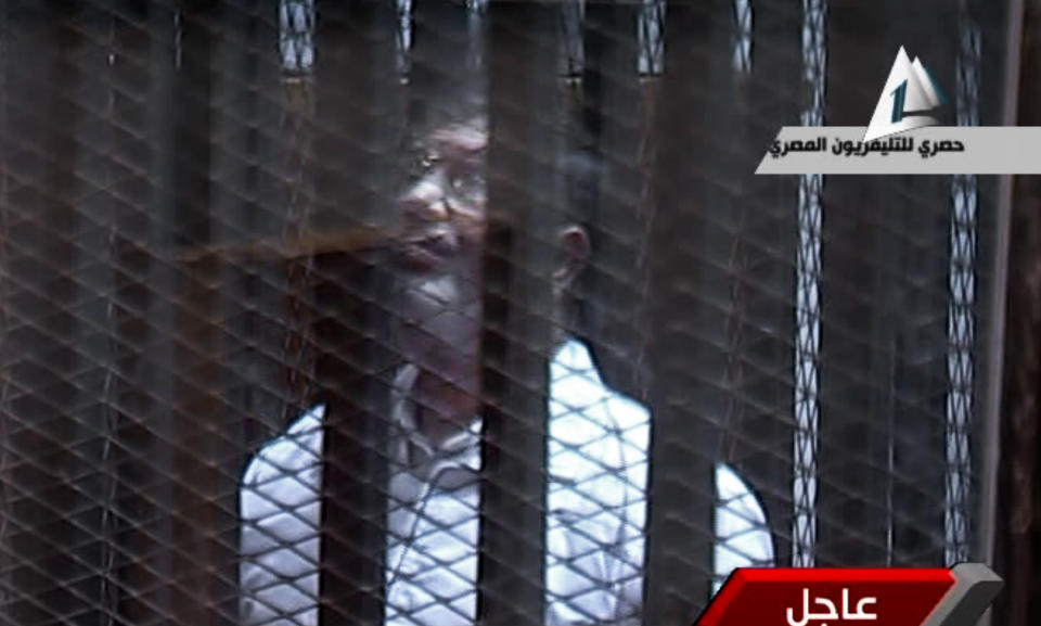 In this image taken from Egypt State TV, Egypt's toppled President Mohammed Morsi stands inside a glass-encased metal cage in a courtroom in Cairo, Egypt, Tuesday, Jan. 28. 2014. Morsi was, separated from other defendants for the start of a new trial Tuesday over charges from prison breaks during the country's 2011 revolution, state television reported. (AP Photo/Egyptian State TV)