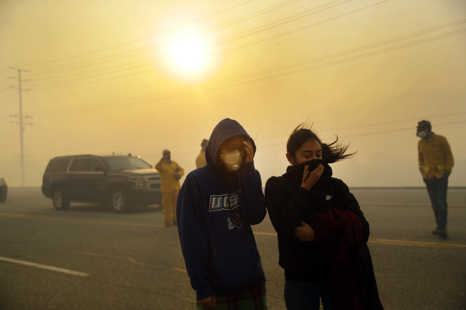 Natalie Acosta, left, and Lea Rivera cover their faces from the smoke created by the Easy Fire Wednesday, Oct. 30, 2019, in Simi Valley, Calif. Driven by powerful Santa Ana winds, the brush fire broke out before dawn between the cities of Simi Valley and Moorpark north of Los Angeles and exploded to more than 1,300 acres (526 hectares), threatening 6,500 homes, Ventura County officials said. (AP Photo/Marcio Jose Sanchez)