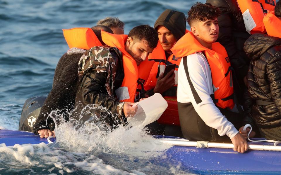 A man pours water out of a small boat as the crowded vessel heads towards Dover - PA