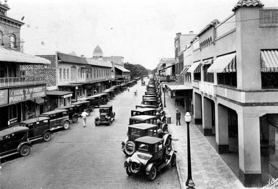 A view looking south along 12th Street West from 4th Avenue where multiple residents and visitors have parked their cars. Businesses like The Howard and Perry Furniture Company and the Fletcher Insurance Company line the east side of 12th street. Courtesy of Manatee County Library archives