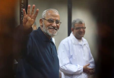 Muslim Brotherhood's Supreme Guide Mohamed Badie (L) flashes the Rabaa sign as he stands behind bars during his trial with ousted Egyptian President Mohamed Mursi and other leaders of the brotherhood at a court in the police academy on the outskirts of Cairo December 14, 2014. REUTERS/Asmaa Waguih