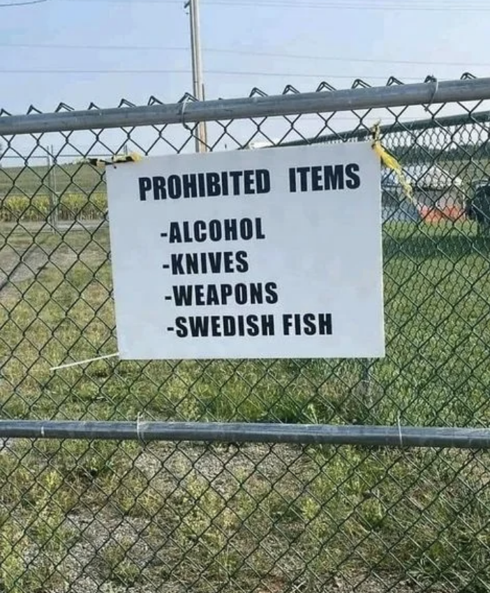 A sign on a chain-link fence lists prohibited items: alcohol, knives, weapons, and Swedish Fish