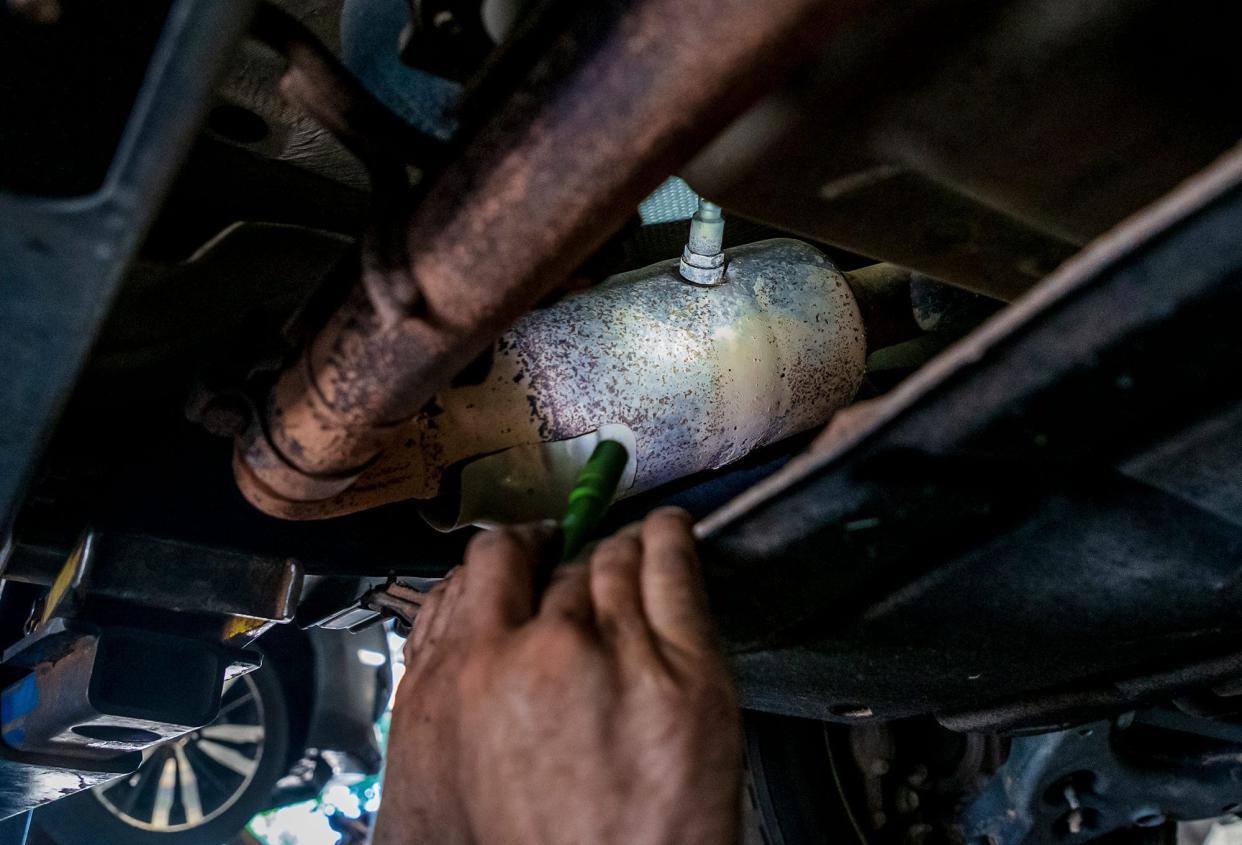 A mechanic points out a catalytic converter.