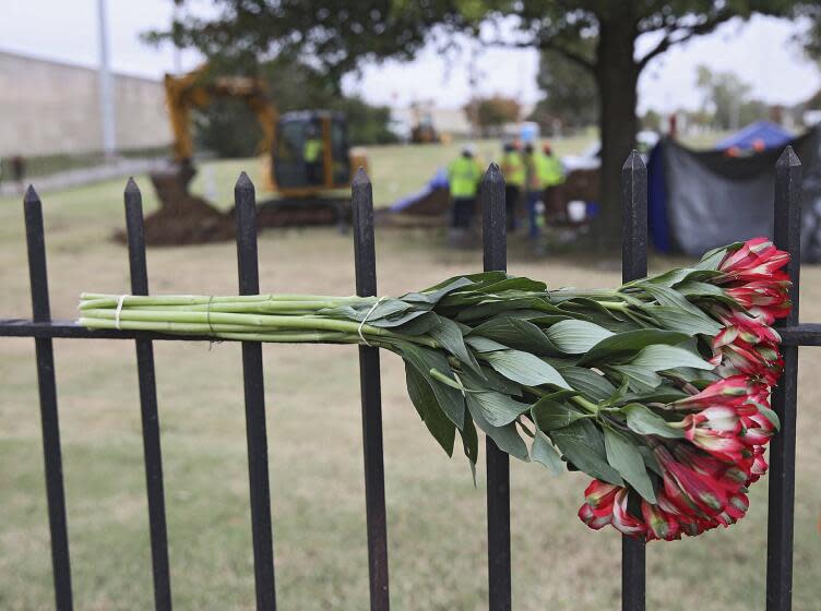 Flowers left by a mourner hang on a fence as crews work on a second test excavation and core sampling in the search for remains at Oaklawn Cemetery from the 1921 Tulsa Race Massacre Wednesday, Oct. 21, 2020. (Mike Simons/Tulsa World via AP)