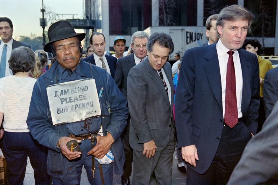 Donald Trump, far right, walks down Fifth Avenue in New York past a beggar after holding a news conference on Nov. 16, 1990. Trump announced he had reached a deal that will temporarily put&nbsp;his Taj Mahal casino into bankruptcy protection.