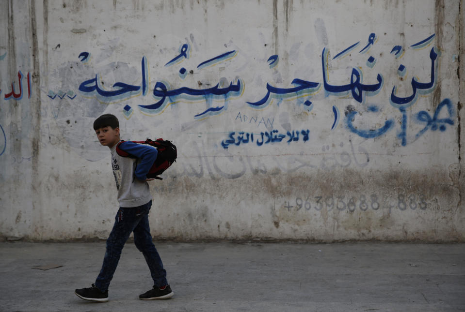 In this March 29, 2018 photo, a Syrian student walks next a wall with Arabic that reads: "We will not emigrate we will confront, no to the Turkish occupation," in Manbij, north Syria. On Friday, Dec. 28, 2018, Syria's military said it entered the flashpoint Kurdish-held town of Manbij, where Turkey has threatened an offensive -- a claim that was refuted by U.S. troops who patrol the town. The announcement and the conflicting reports reflect the potential for chaos in the wake of the U.S. surprise decision to withdraw troops from Syria. (AP Photo/Hussein Malla)