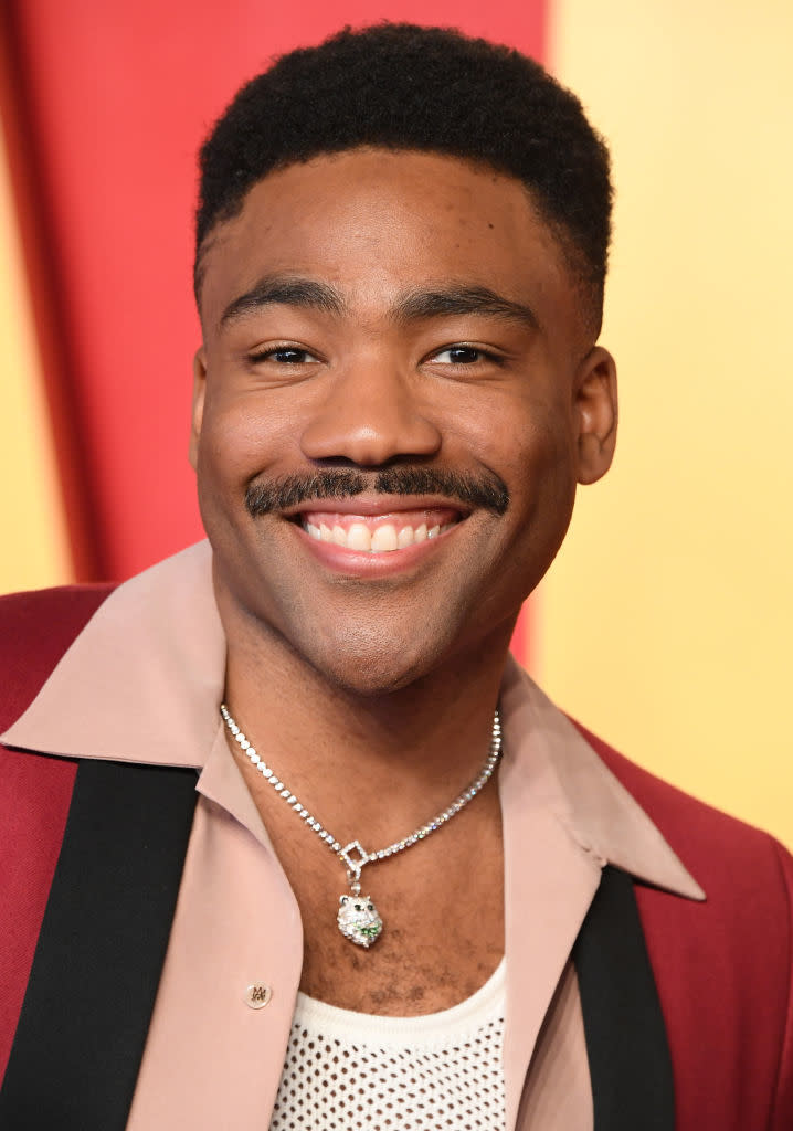 Donald smiling for the camera, wearing a necklace with a green pendant and a casual blazer over a shirt