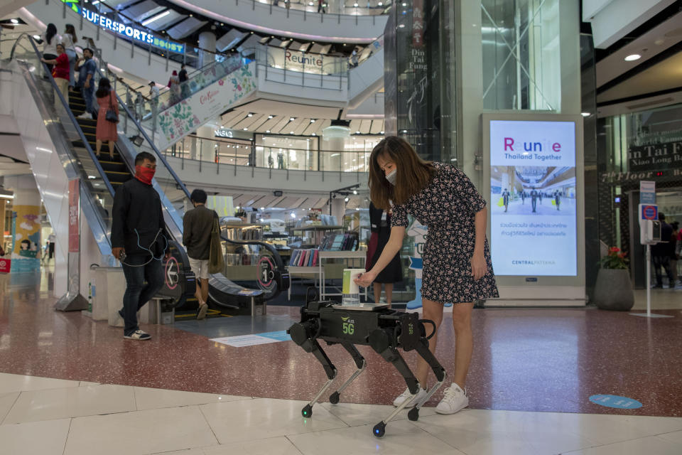 A woman disinfects her hands from a mobile robot that carries a container of sanitization liquid at Central World, an upmarket shopping mall in Bangkok, Thailand, Wednesday, May 27, 2020. Thai government continues to ease restrictions related to running business in capital Bangkok that were imposed weeks ago to combat the spread of COVID-19. (AP Photo/Gemunu Amarasinghe)