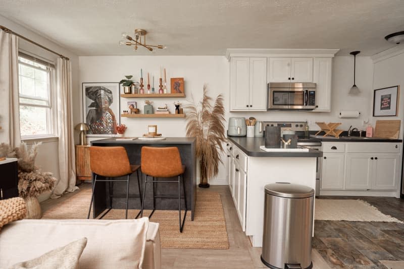 View of dining and kitchen area from living room in white apartment with lots of warm accents