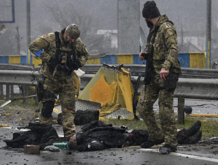 Ukrainian soldiers stand near dead bodies on a highway in Bucha.