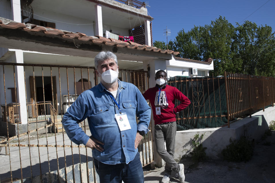 In this photo taken on Monday, April 27, 2020, father Daniele Moschetti, left, and Appiah Kwasi from Ghana, a cultural mediator, wait for a resident as they bring food to the people of Castel Volturno, near Naples, Southern Italy. Father Daniele Moschetti spent a decade doing missionary work in the slums of Nairobi and now he finds his work to be similar in his own country. They are known as “the invisibles,” the undocumented African migrants who, even before the coronavirus outbreak plunged Italy into crisis, barely scraped by as day laborers, prostitutes and seasonal farm hands. Locked down for two months in their overcrowded apartments, their hand-to-mouth existence has grown even more precarious with no work, no food and no hope. (AP Photo/Alessandra Tarantino)