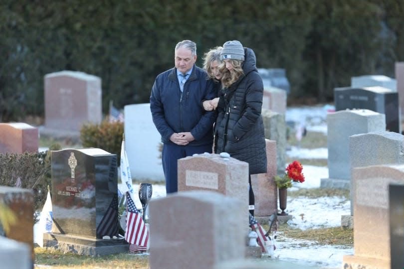 Cindy Chesna stands at the Blue Hills Cemetery grave in Braintree of her late husband, Weymouth police Sgt. Michael Chesna, after a jury found the shooter guilty at his second trial on Friday, Feb. 16, 2024. With Chesna is her sister, Debbie Comperchio, and Debbie's husband.