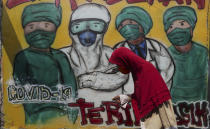 A woman wears a face mask to help curb the spread of the new coronavirus past a coronavirus awareness mural at Rawa Pasung village in Bekasi on the outskirts of Jakarta, Indonesia, Thursday, July 23, 2020. (AP Photo/Achmad Ibrahim)