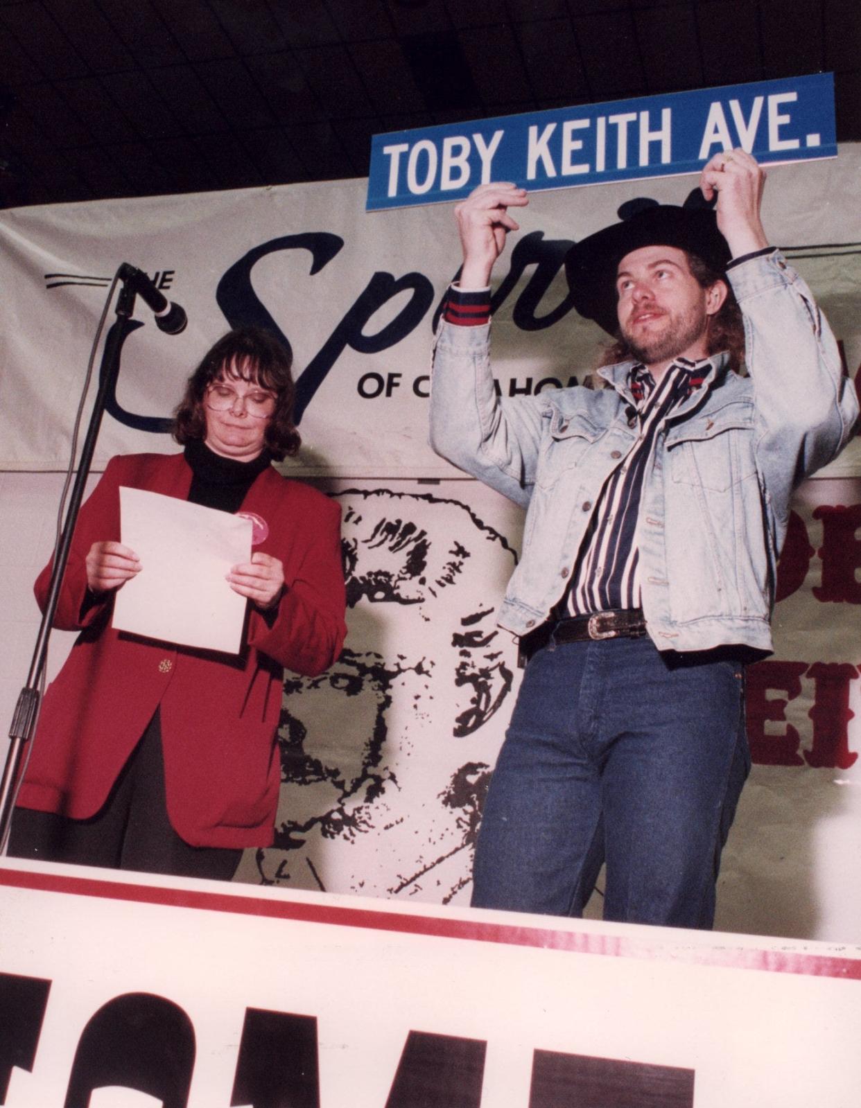 In March 1994, country music singer Toby Keith holds a street sign named in his honor. Moore Mayor Debe Homer had presented Keith the sign during a ceremony at Moore High School.