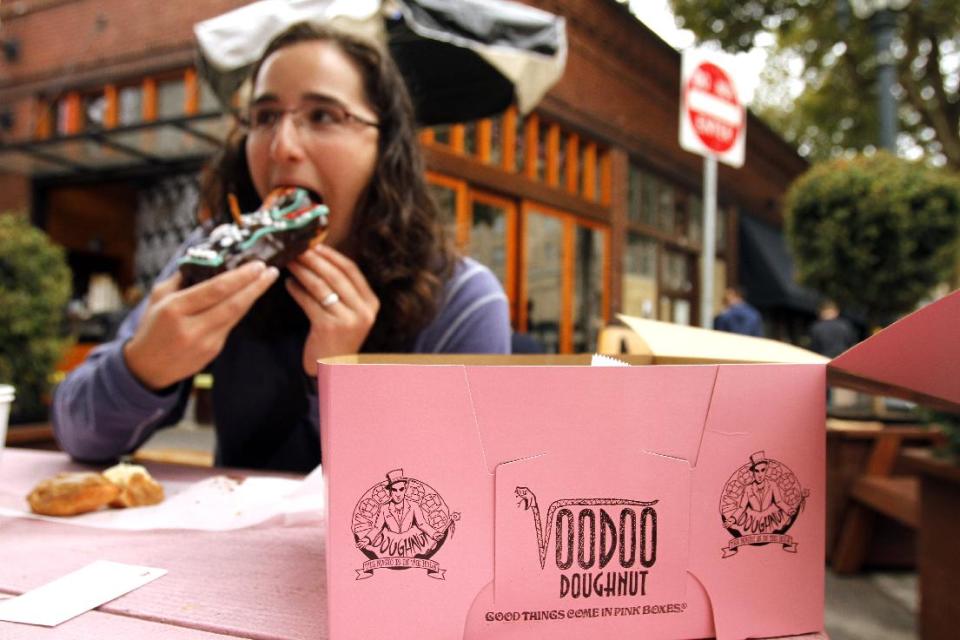 Jennie Myren, who is from Iowa and spending her honeymoon in Portland, enjoys the signature doughnut shaped like a voodoo doll with a pretzel stick stake through its' heart outside the famous Voodoo Doughnuts shop in downtown Portland, Ore., Wednesday, Sept. 19, 2012. Researchers at Portland State University found that the Portland atmosphere and culture is a magnet for the young and college educated, even though a disproportionate share of them are working in part-time jobs or positions that don’t require a college degree. (AP Photo/Don Ryan)
