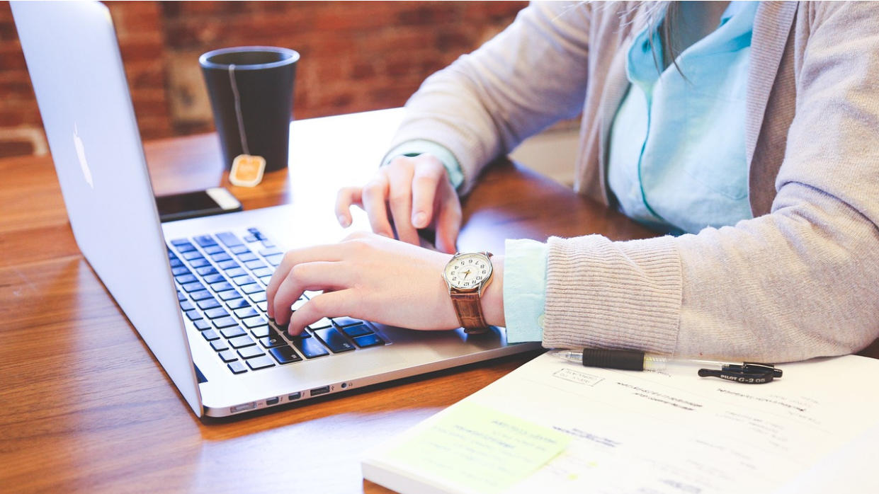   Woman working on laptop, with coffee cup . 