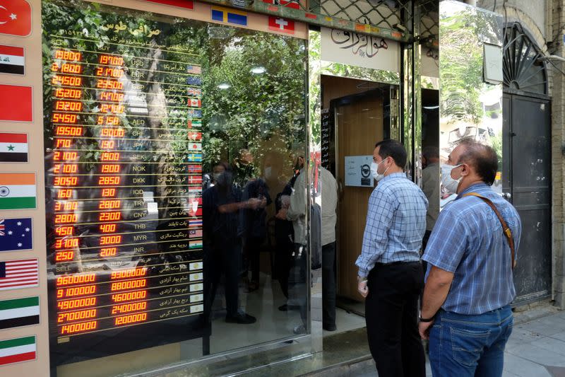 People wear protective face masks as they look at the electronic currency board at Ferdowsi square in Tehran