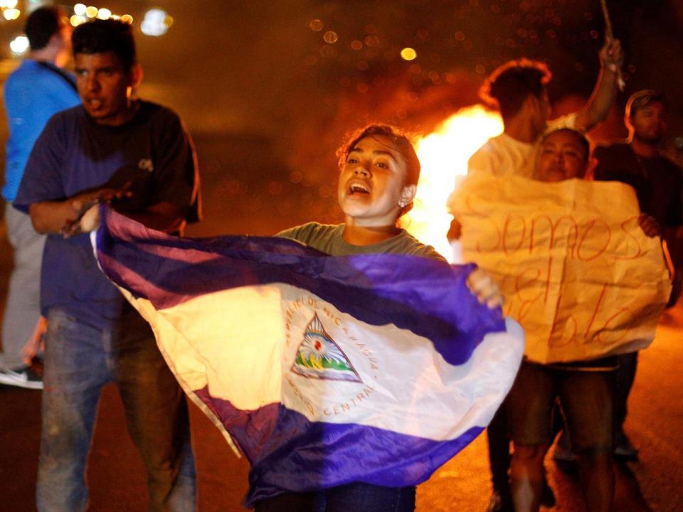 A demonstrator holds up a Nicaragua flag next to a burning barricade as demonstrators take part in a protest over a controversial reform to the pension plans of the Nicaraguan Social Security Institute (INSS) in Managua, Nicaragua (REUTERS/Jorge Cabrera)