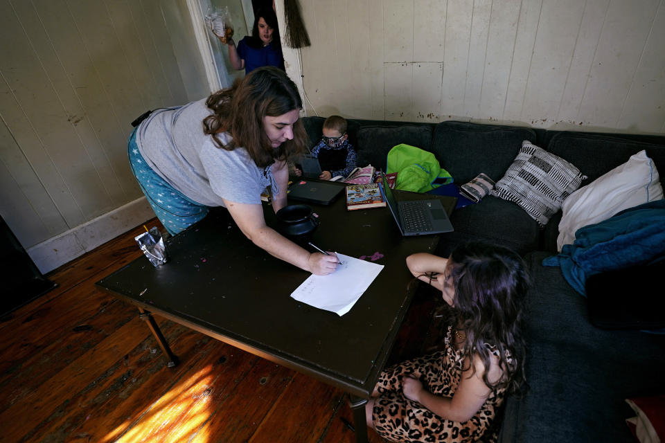 Christi Brouder, left, reviews multiplication tables with her daughter Elena while assisting her children with remote learning due to the COVID-19 outbreak, in a makeshift classroom in the living room at the family home, Wednesday, Oct. 14, 2020, in Haverhill, Mass. Brouder has four children that are distance learning. Many families with multiple students, some with special needs, are dealing with the challenges of remote distance learning in their home. (AP Photo/Charles Krupa)