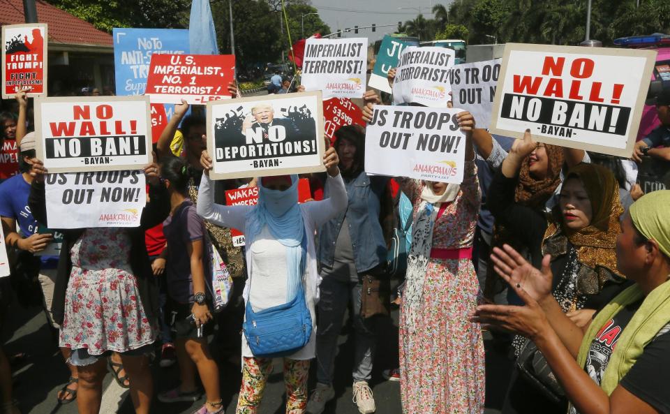 Protesters display placards in front of riot police during a rally at the U.S. Embassy to protest U.S. President Donald Trump's recent anti-immigration policies, Saturday, Feb. 4, 2017, in Manila, Philippines. The protest also marked the Feb. 4, 1899 Filipino-American War. (AP Photo/Bullit Marquez)