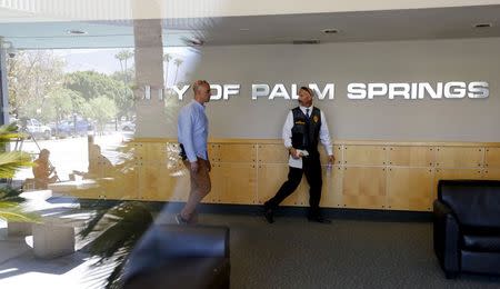 Investigators walk through the lobby of Palm Springs City Hall while news media are reflected on glass during a raid on the city's offices in Palm Springs, California, September 1, 2015. REUTERS/Sam Mircovich