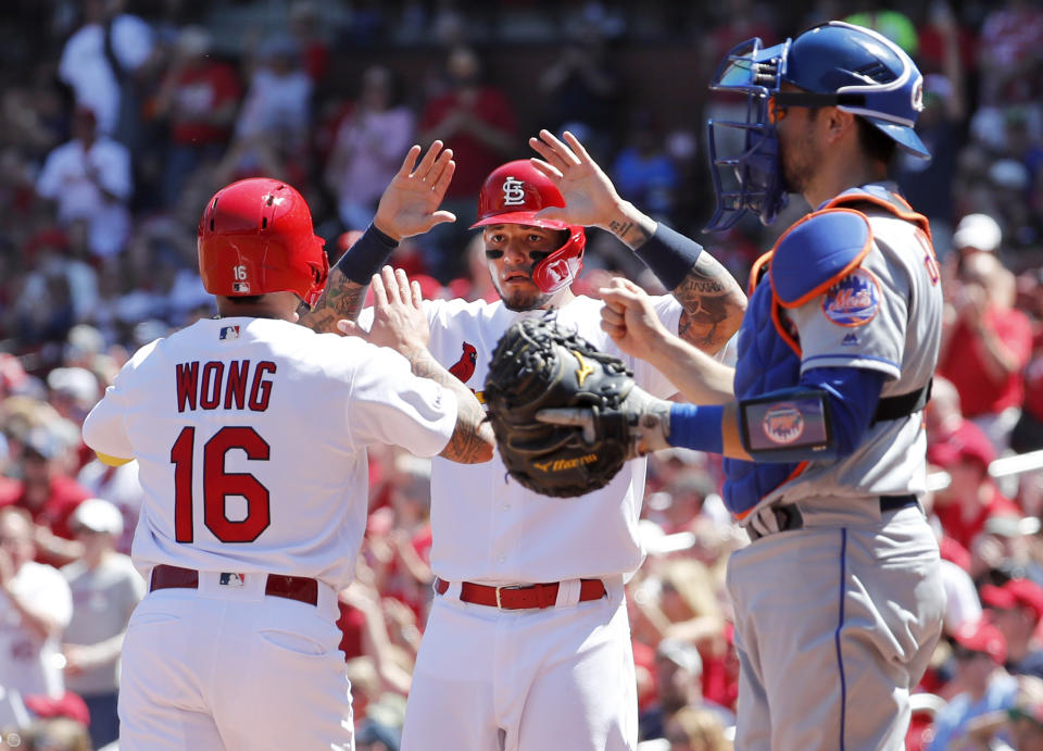 St. Louis Cardinals' Kolten Wong, left, and teammate Yadier Molina celebrate after scoring past New York Mets catcher Travis d'Arnaud, right, during the second inning of a baseball game Sunday, April 21, 2019, in St. Louis. (AP Photo/Jeff Roberson)